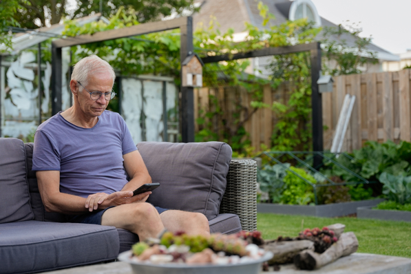 Man kijkt in zijn tuin op zijn telefoon naar de HR Energy app, waarmee hij de prestaties van zijn PVT-systeem kan bekijken.