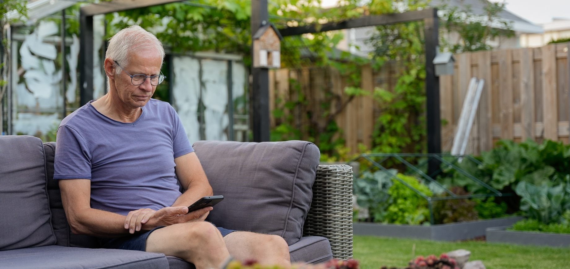 Man kijkt in zijn tuin op zijn telefoon naar de HR Energy app, waarmee hij de prestaties van zijn PVT-systeem kan bekijken.