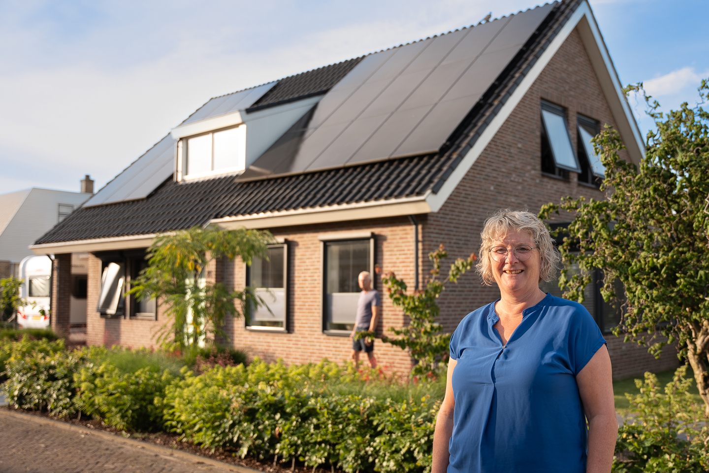 Vrouw voor haar huis met op het dak PVT-panelen van HR Energy, onderdeel van een duurzaam PVT-systeem met warmtepomp.