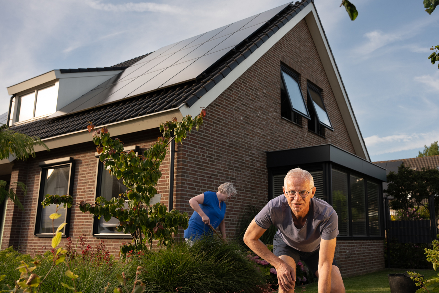 Man en vrouw in hun tuin en op de achtergrond hun dak met PVT panelen van HR energy