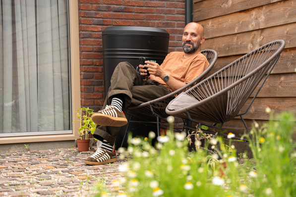 Man zit in zijn tuin, kijkt op zijn telefoon naar HR Energy app, waarmee hij de prestaties van zijn PVT-systeem kan bekijken.