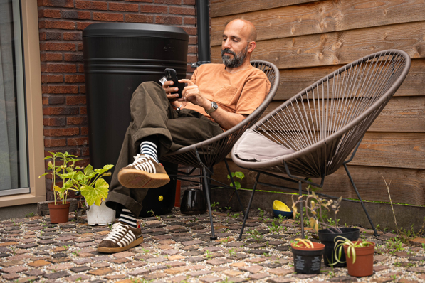 Man in zijn tuin die kijkt op zijn telefoon naar de HR energy app om zijn warmtepomp te monitoren