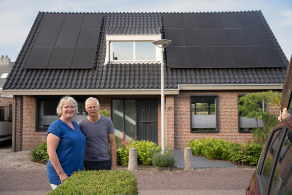 Voor hun huis staat een stel, op het dak zijn PVT-panelen van HR Energy te zien, onderdeel van PVT-systeem met warmtepomp.